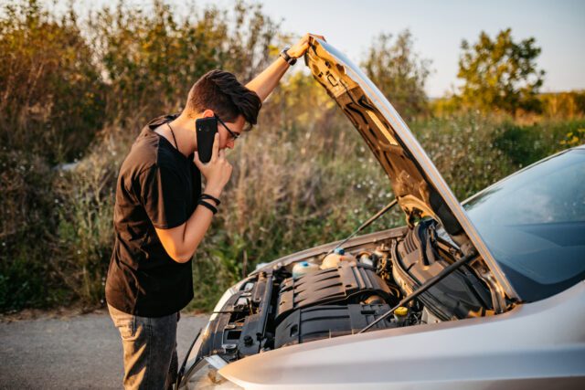 Un jeune homme caucasien, beau et élégant, est en panne de voiture et appelle l'assistance routière