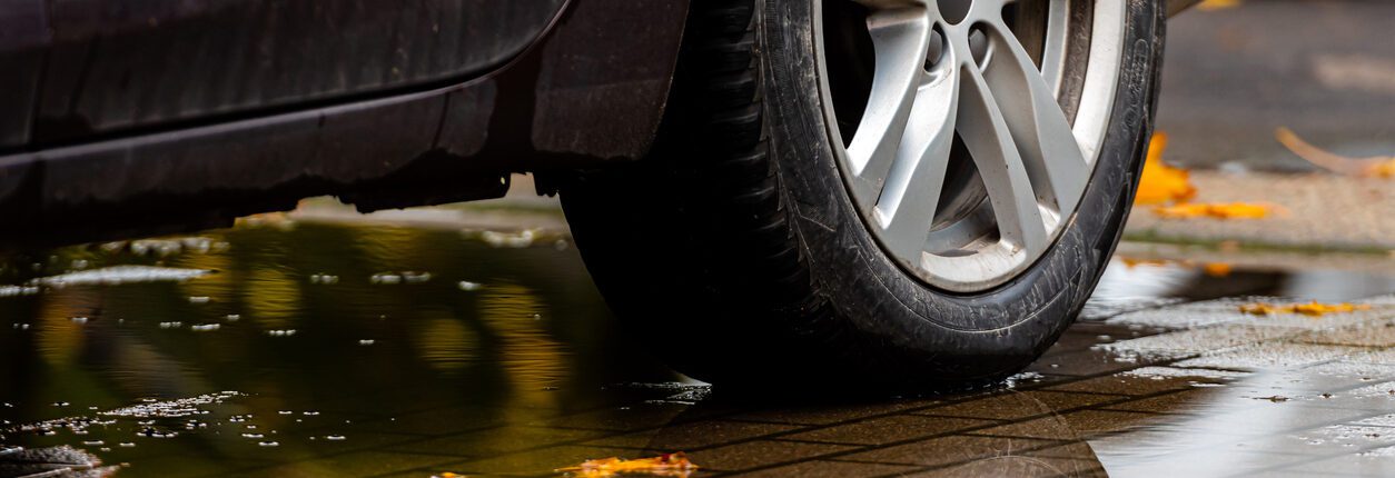 Gros plan sur un pneu arrière de voiture roulant sur une flaque d'eau avec des feuilles d'automne