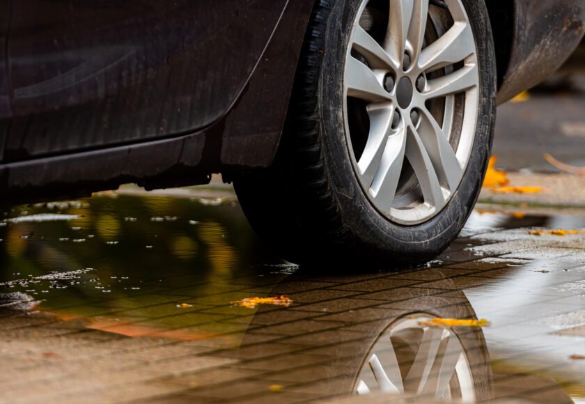 Gros plan sur un pneu arrière de voiture roulant sur une flaque d'eau avec des feuilles d'automne