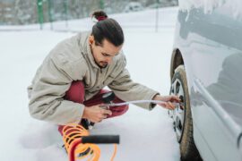 Jeune homme vérifiant la pression des pneus en hiver